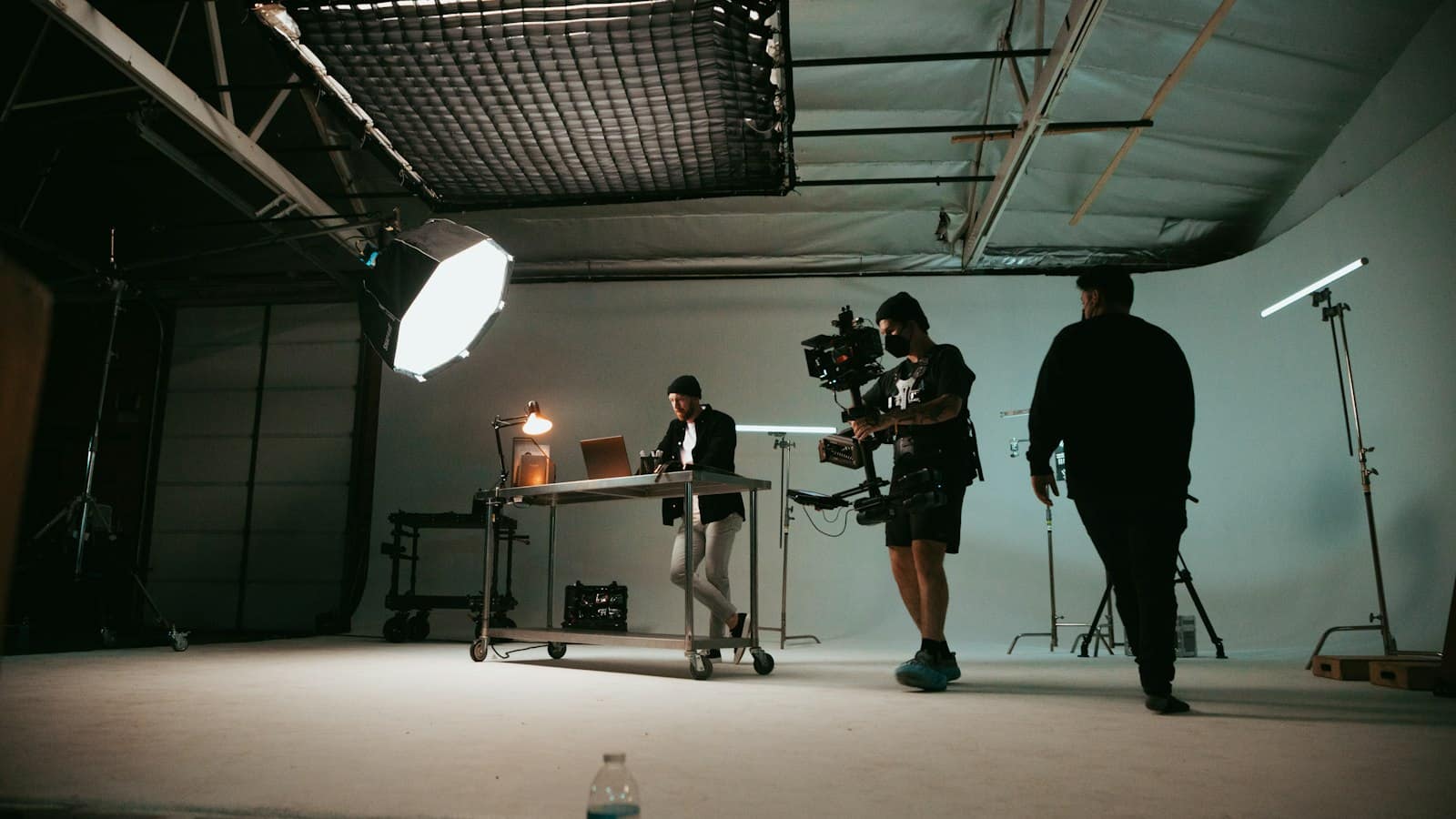 A film crew with a camera rig shooting a man at a desk in a lit studio