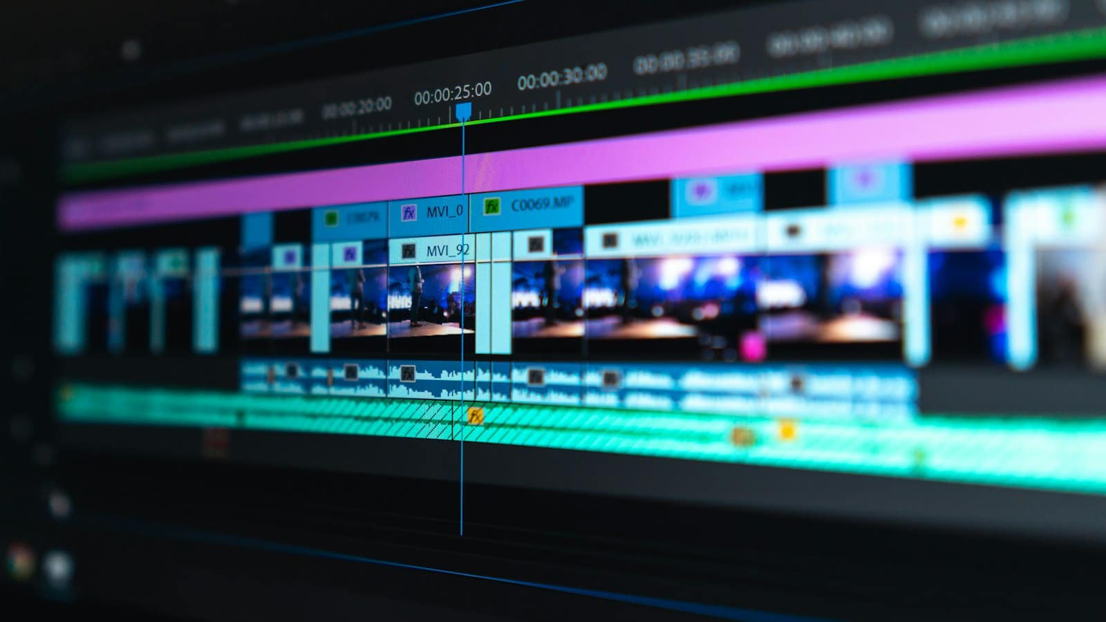 A video editing timeline on a monitor, with clips and an audio track in blue, purple and green