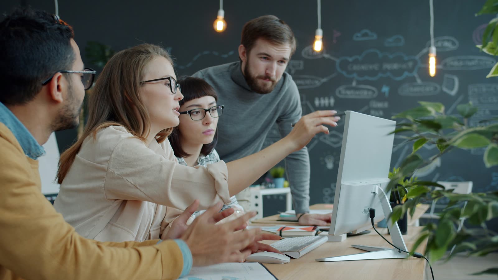 Four colleagues gathered around a desktop computer in an office, one pointing at the screen